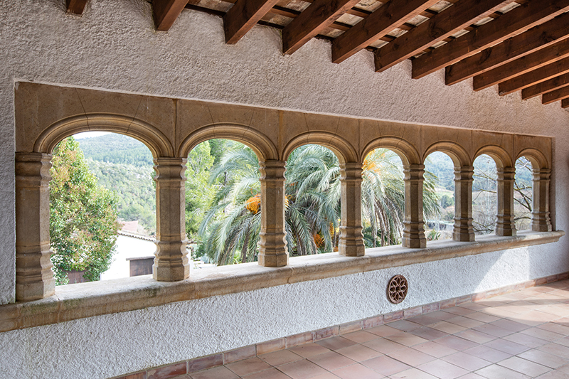 Galería de arcos de piedra de Masia Torreblanca, con vigas de madera y palmeras